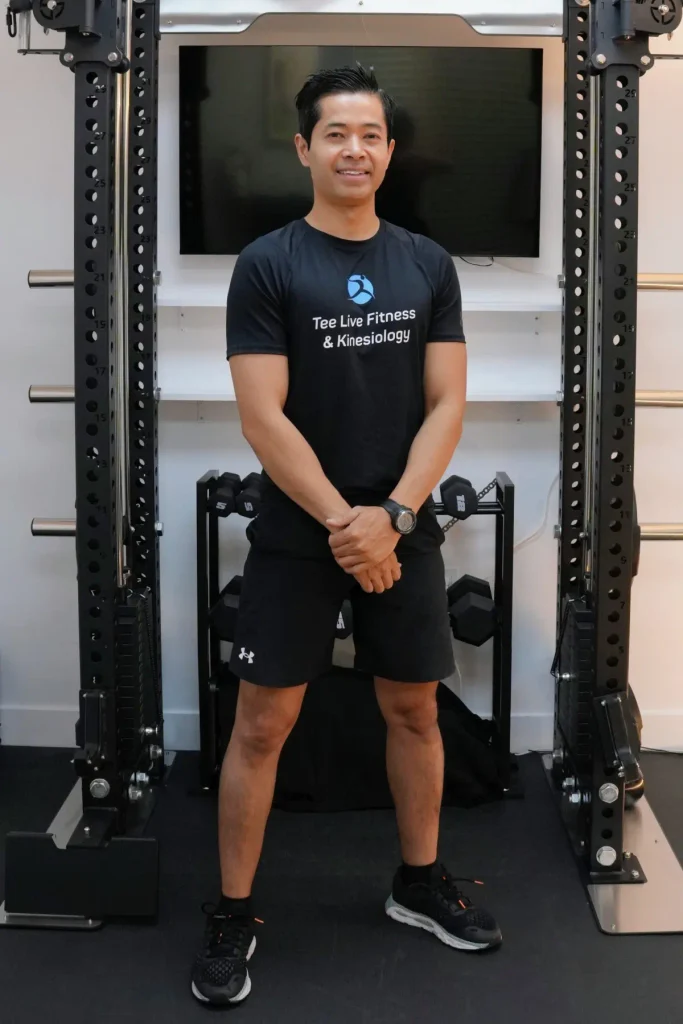 Kinesiologist and personal trainer Tee Live from Tee Live Fitness And Kinesiology standing in front of fitness equipment.