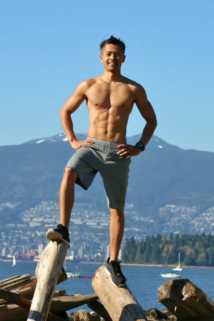 Personal trainer and kinesiologist Tee Live from Tee Live Fitness And Kinesiology wearing grey shorts standing in logs at the beach.